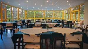A spacious indoor dining area with multiple tables and chairs, large windows, and a view of trees outside. - Varshava Hotel (Golden Sands)