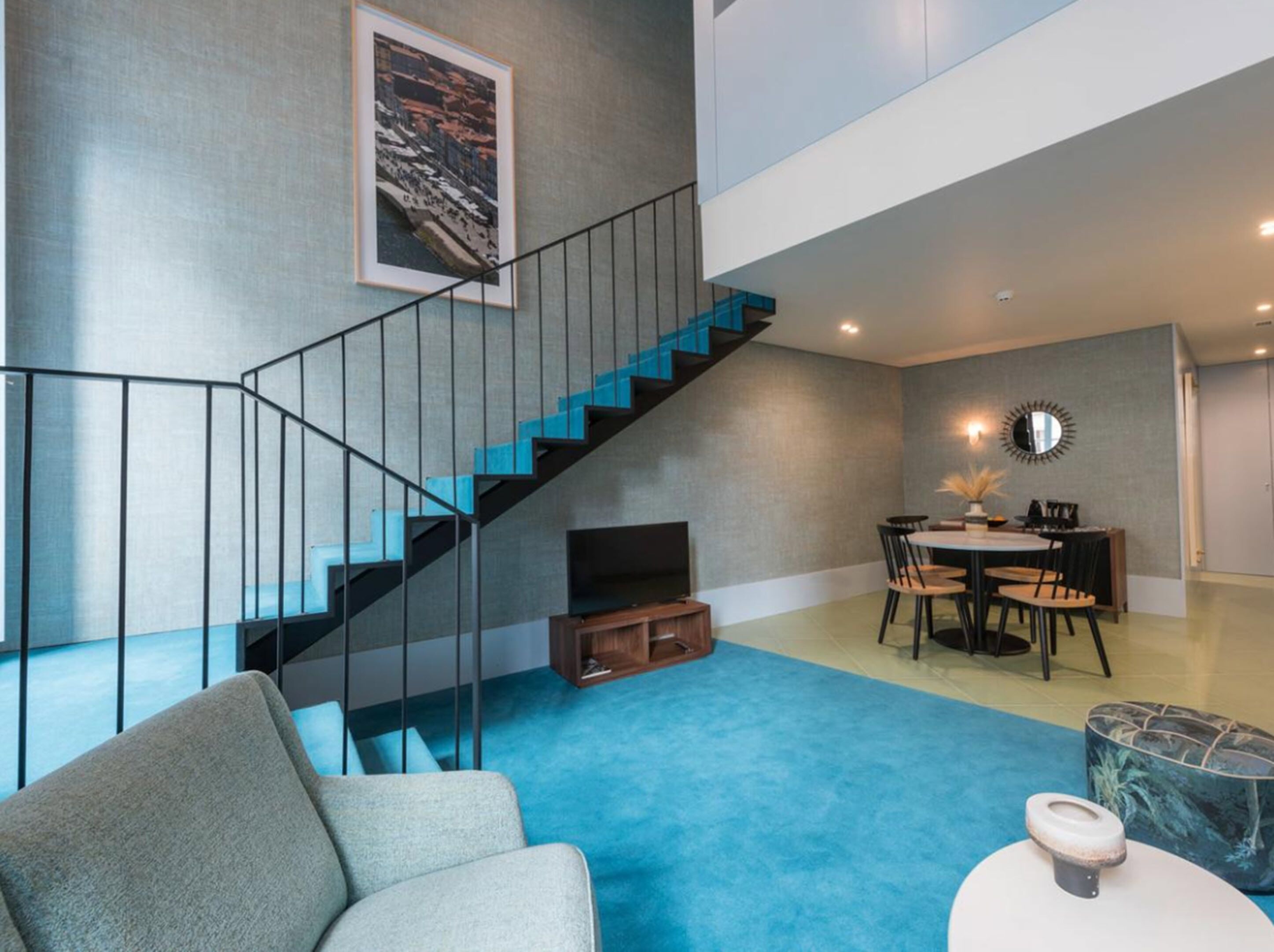 A modern living space with a staircase, a dining area, and a blue carpet.