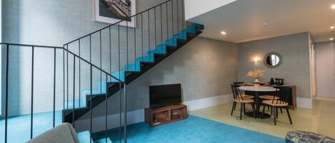 A modern living space with a staircase, a dining area, and a blue carpet.
