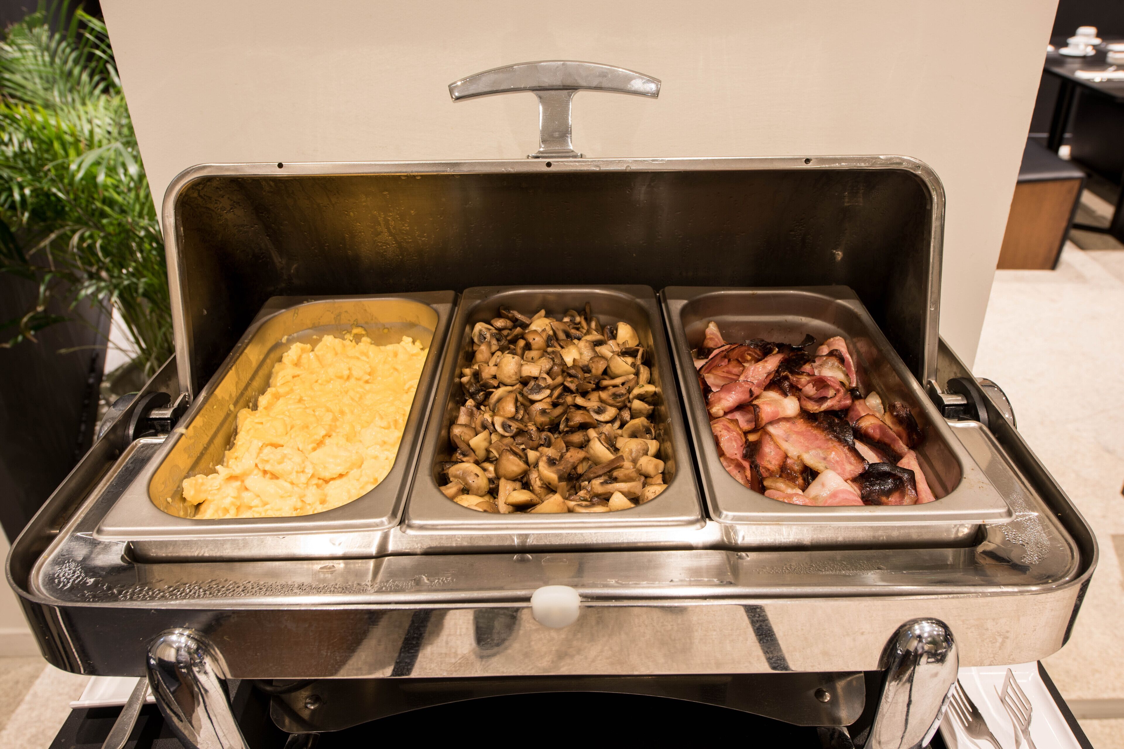 Een buffet met drie schalen eten: roerei, gebakken champignons en spek.