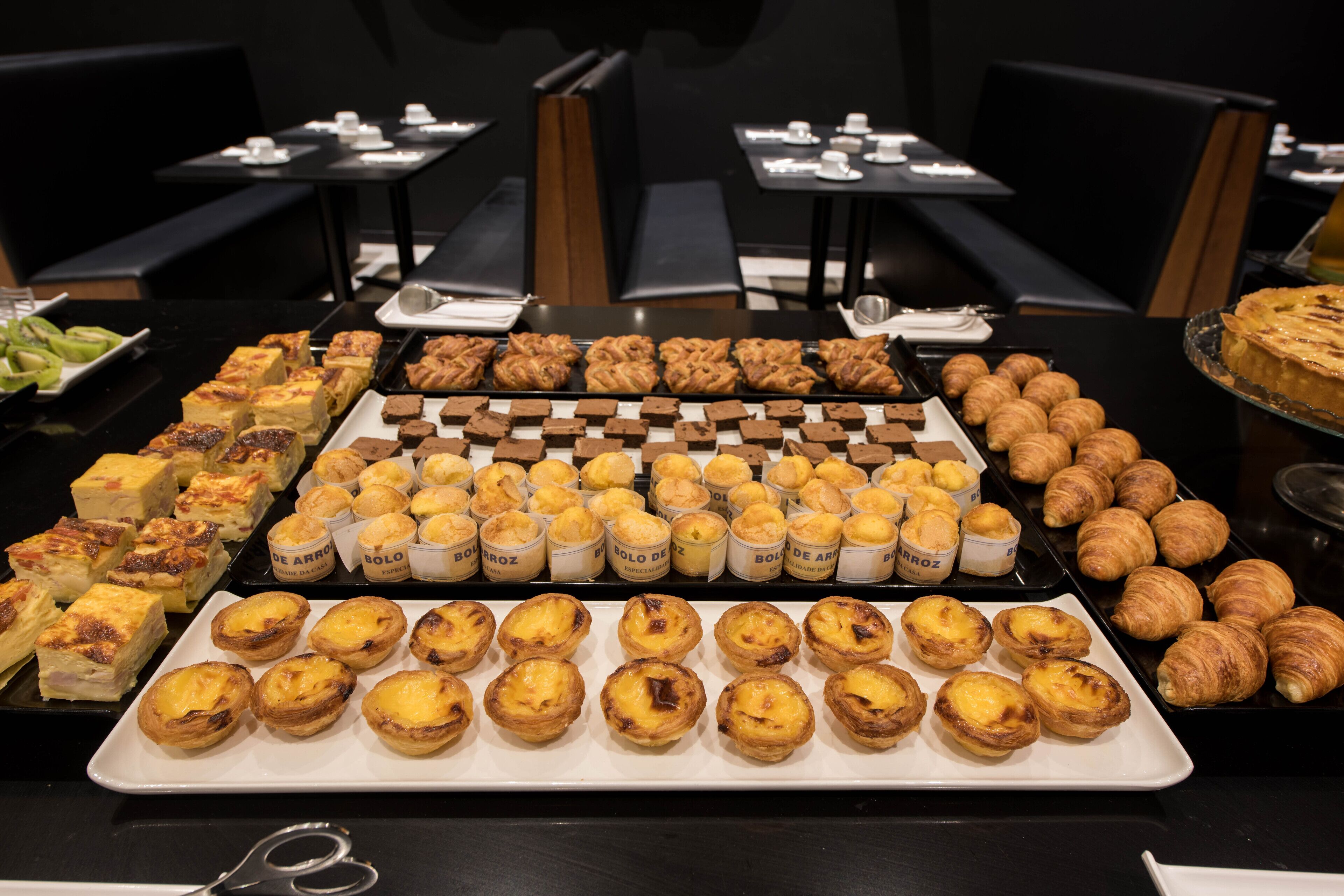 A buffet table with various pastries and desserts, including Portuguese egg tarts and croissants.