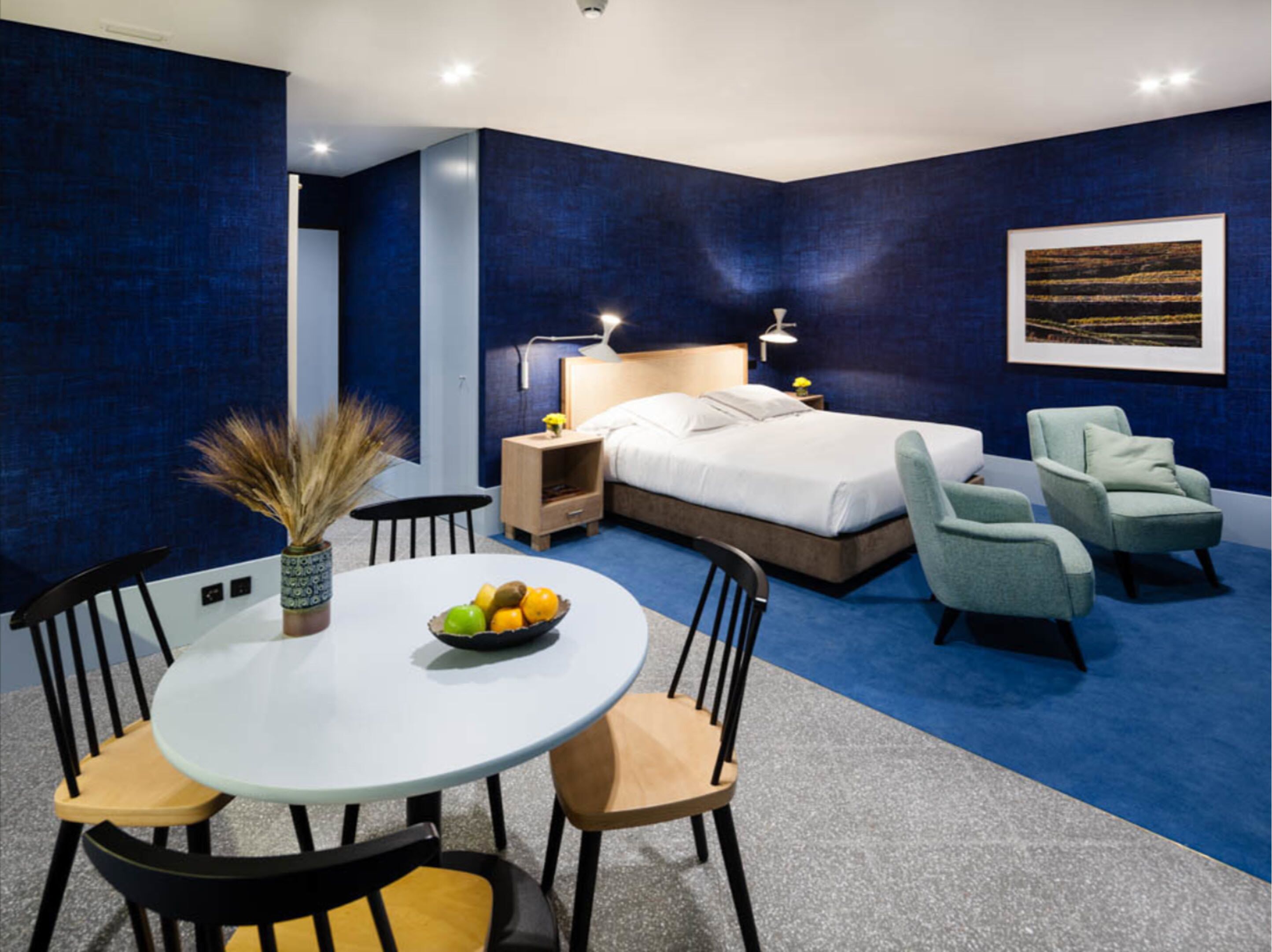 A modern bedroom with a large bed, bedside tables, a desk, and two chairs.