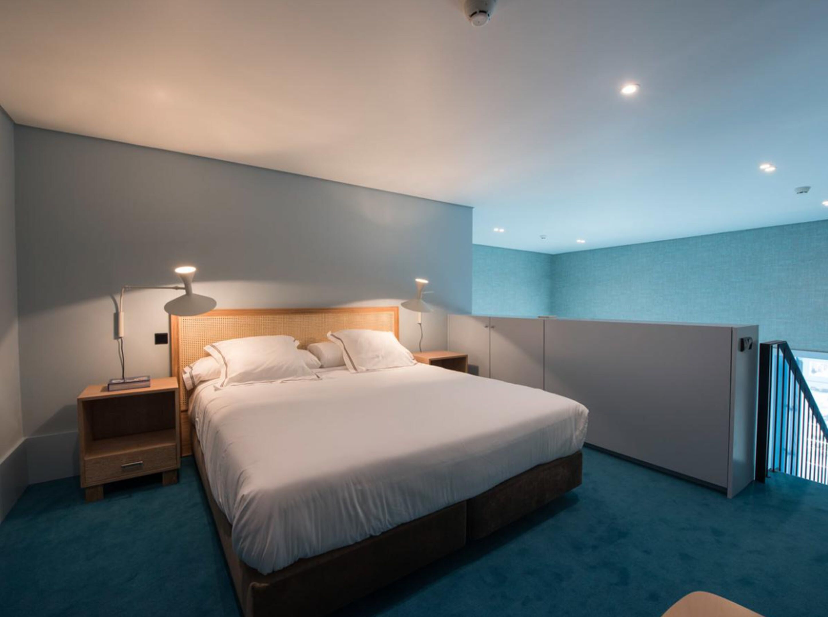 Ein modernes Hotelzimmer mit einem großen Bett, zwei Nachttischen mit Lampen, einem hölzernen Kopfteil und Blick auf den Himmel vom Balkon aus.