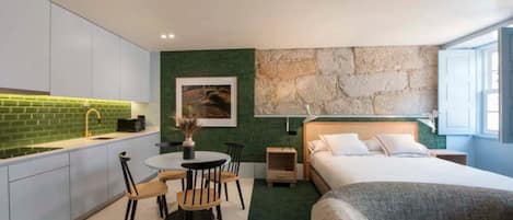 A modern hotel room with a kitchen, a dining area, and a bed.