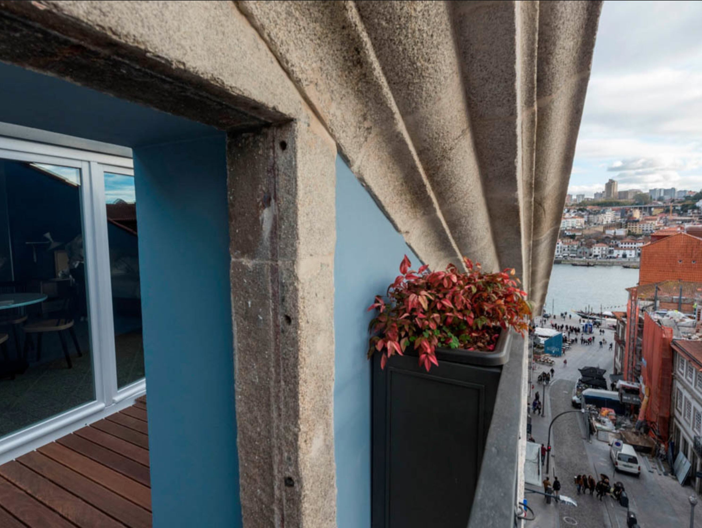 A balcony with a view of a cityscape, a potted plant, and a wooden deck.