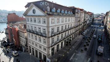 Un immeuble à plusieurs étages, surmonté d’un grand panneau « CH CH », situé dans une rue animée de la ville, avec une rivière en arrière-plan.