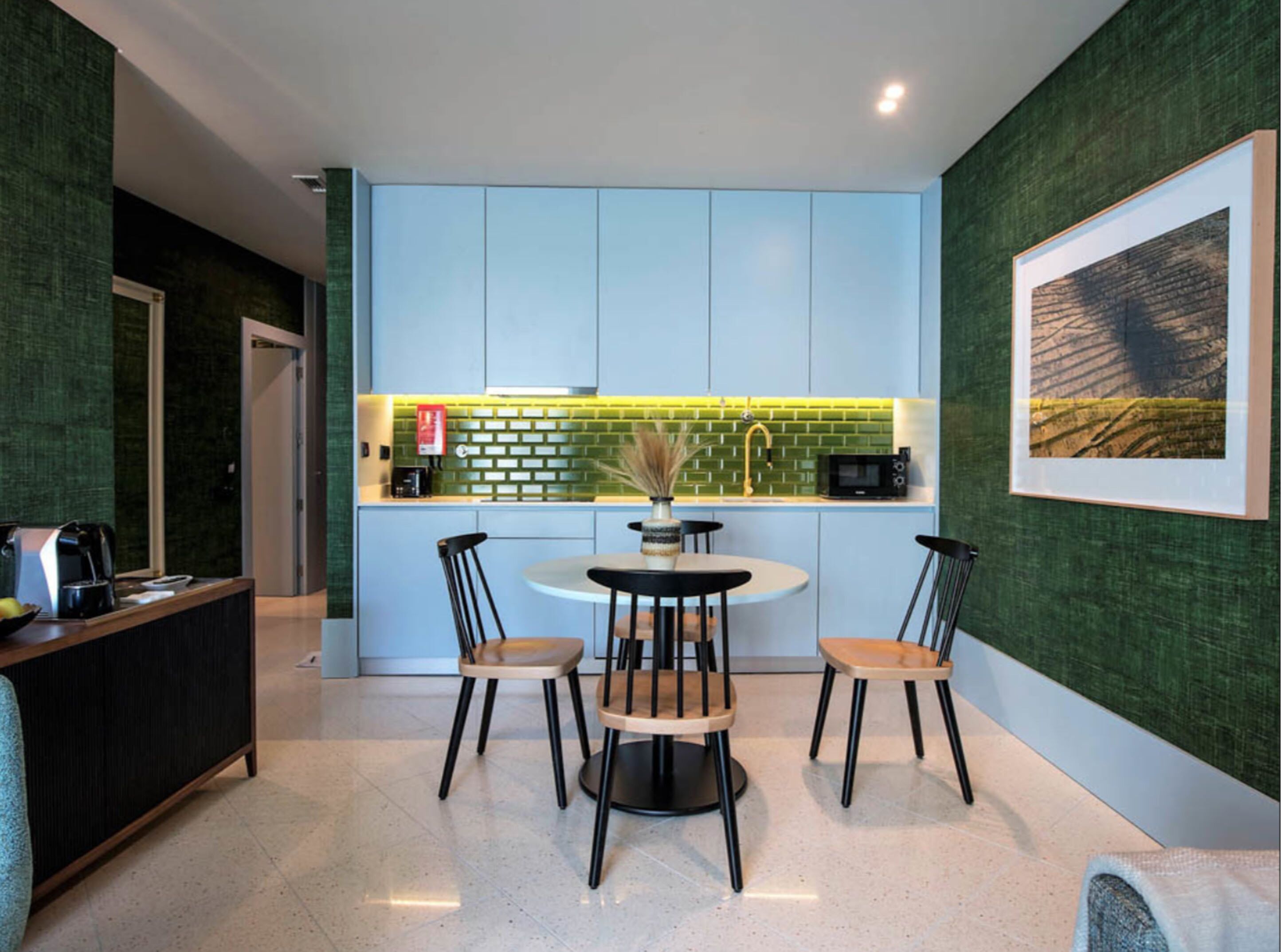 A modern kitchen with a dining area, featuring a round table with four chairs, a coffee machine, and a microwave.