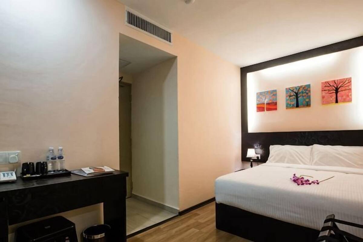 Een hotelkamer met een bed, een bureau met toiletartikelen en drie schilderijen aan de muur.