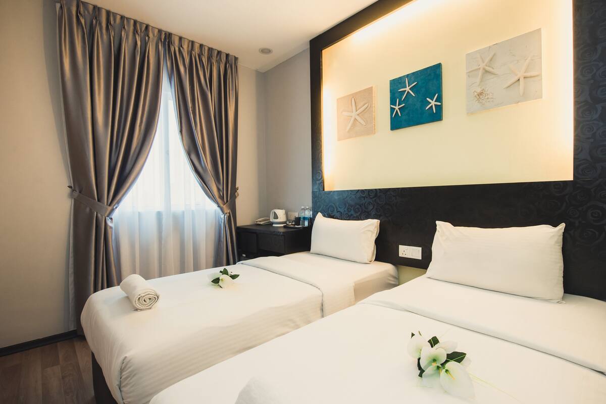 Een hotelkamer met twee bedden, een nachtkastje, een raam met gordijnen en een kunstwerk aan de muur.
