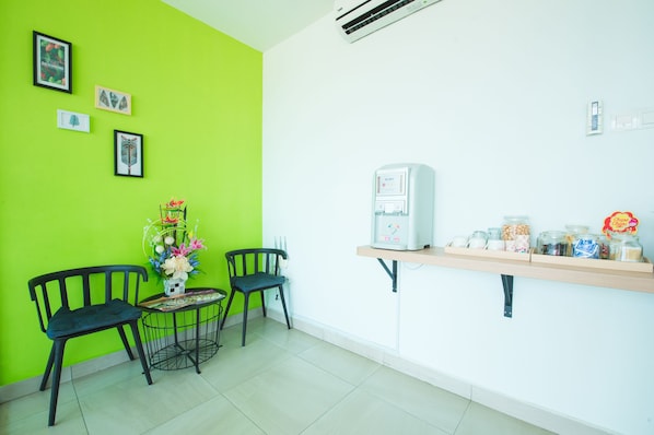 Quarto com duas cadeiras, uma mesinha com um vaso de flores, uma estante com potes e recipientes, e um ar-condicionado fixado na parede.