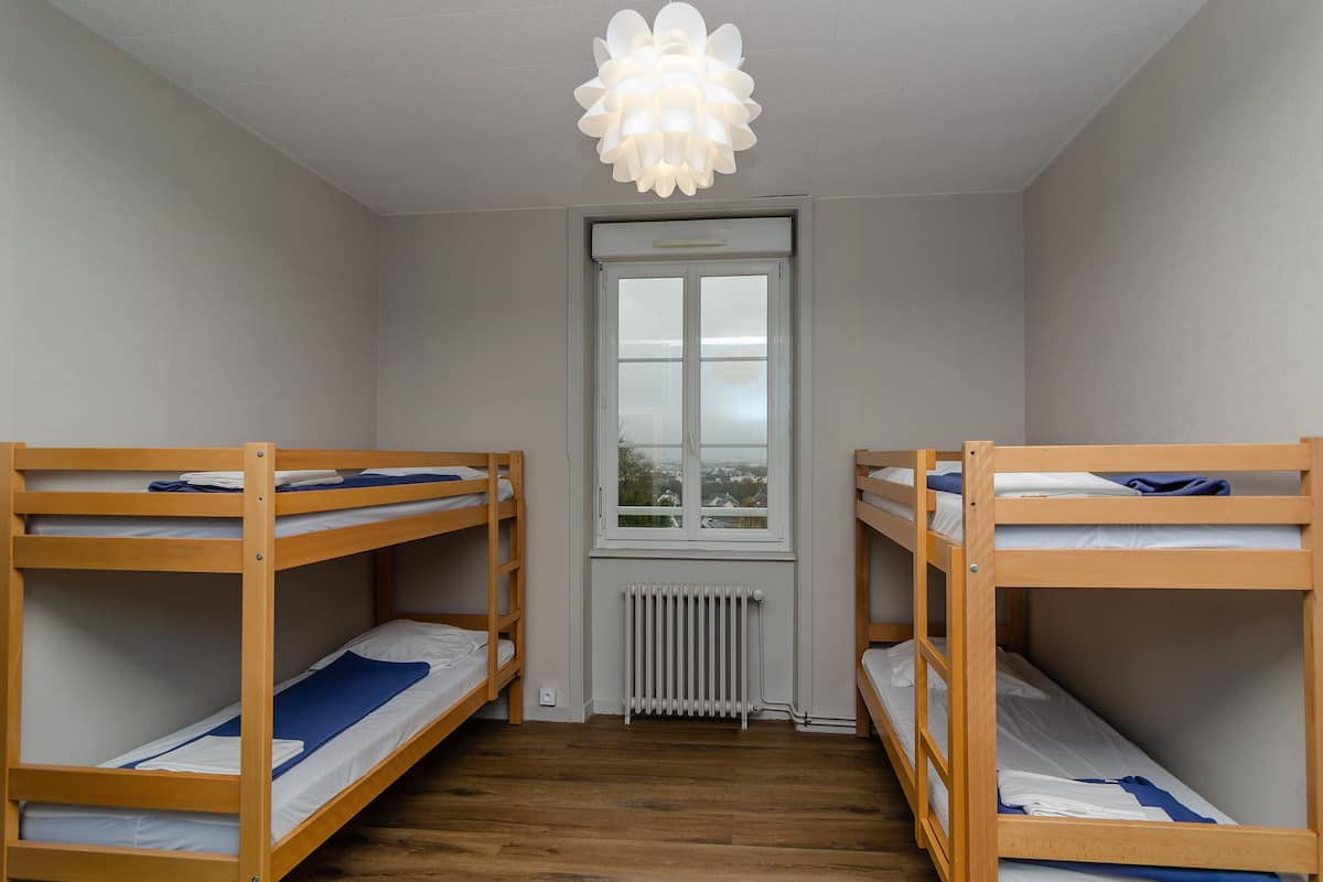 A room with two bunk beds, a radiator, a window, and a ceiling light fixture.