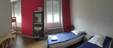 Ein Schlafzimmer mit einem Bett, einem Schreibtisch, einem Stuhl, einem Heizkörper und einem Fenster mit Jalousien.