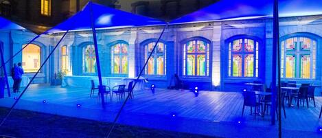 A courtyard with a covered seating area, stone walls, and stained glass windows.