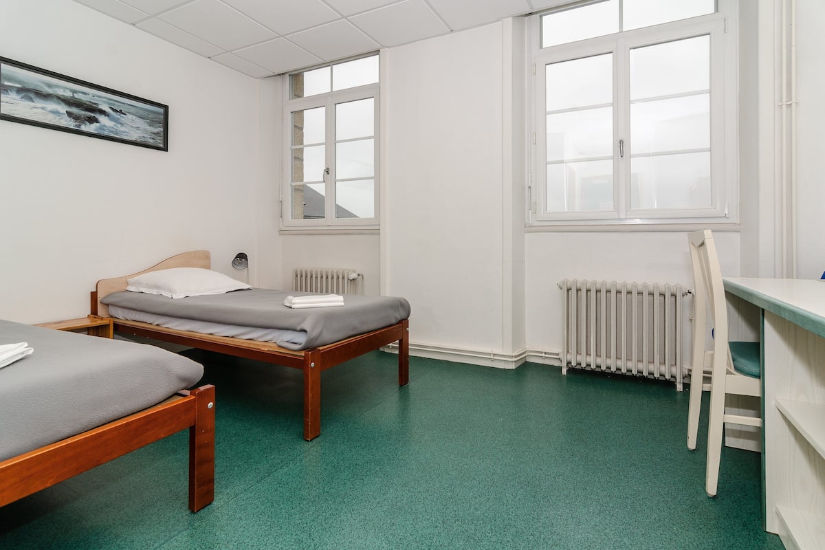 A room with two wooden beds, a desk, a chair, and a radiator.