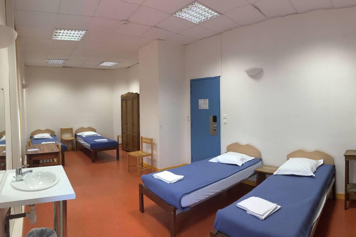 A dormitory room with bunk beds, a single bed, a desk with a sink, and a mirror.