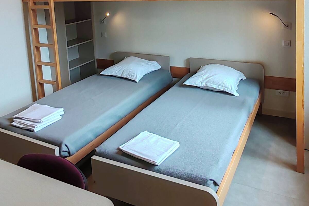 A dormitory room with two single beds, a wooden bunk bed, a desk, and a chair.