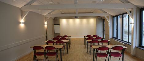 A conference room with wooden flooring, red chairs, and tables arranged in a U-shape.