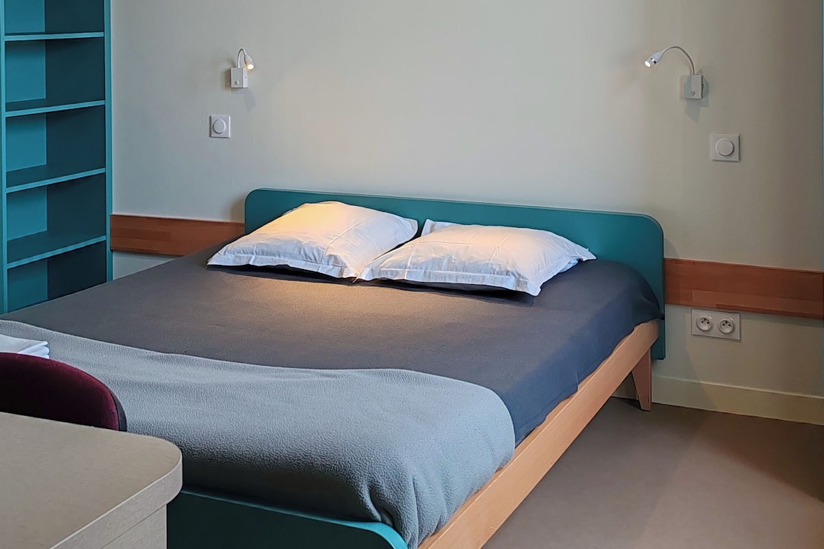 A bedroom with a bed, a teal-colored wardrobe, and a ceiling light fixture.