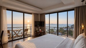 Camera d'albergo con un letto grande, una TV, una scrivania con una sedia e un balcone vista mare.