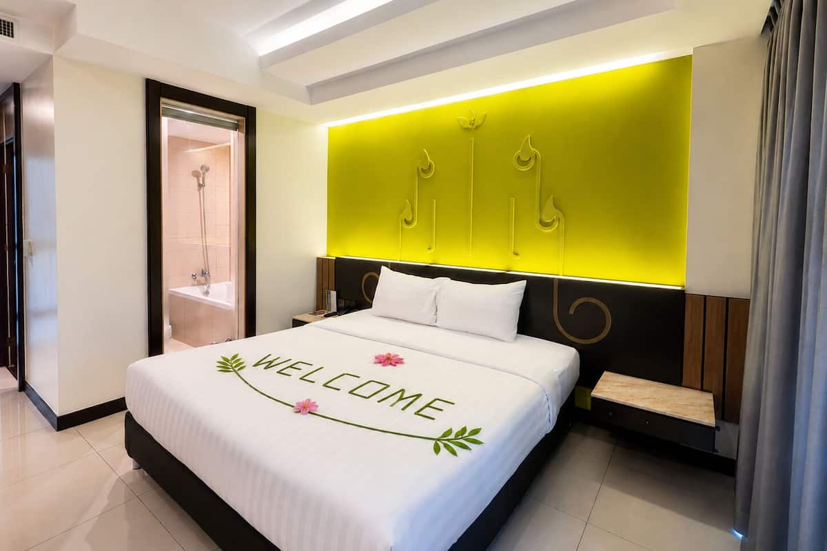 A modern hotel room with a bed, a bedside table, a nightstand, a built-in shower, and a bright accent wall.