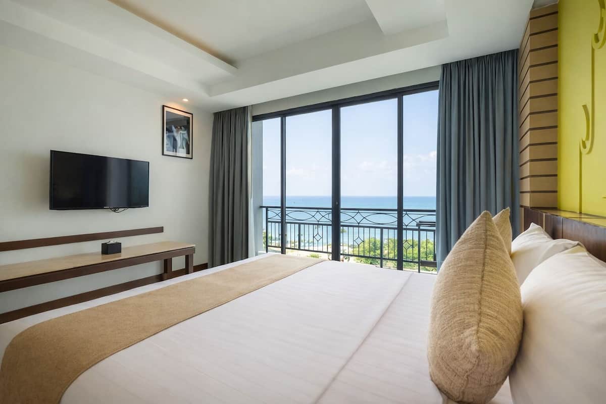 A hotel room with a large bed, a flat-screen TV, a balcony with a view of the sea, and a modern design.