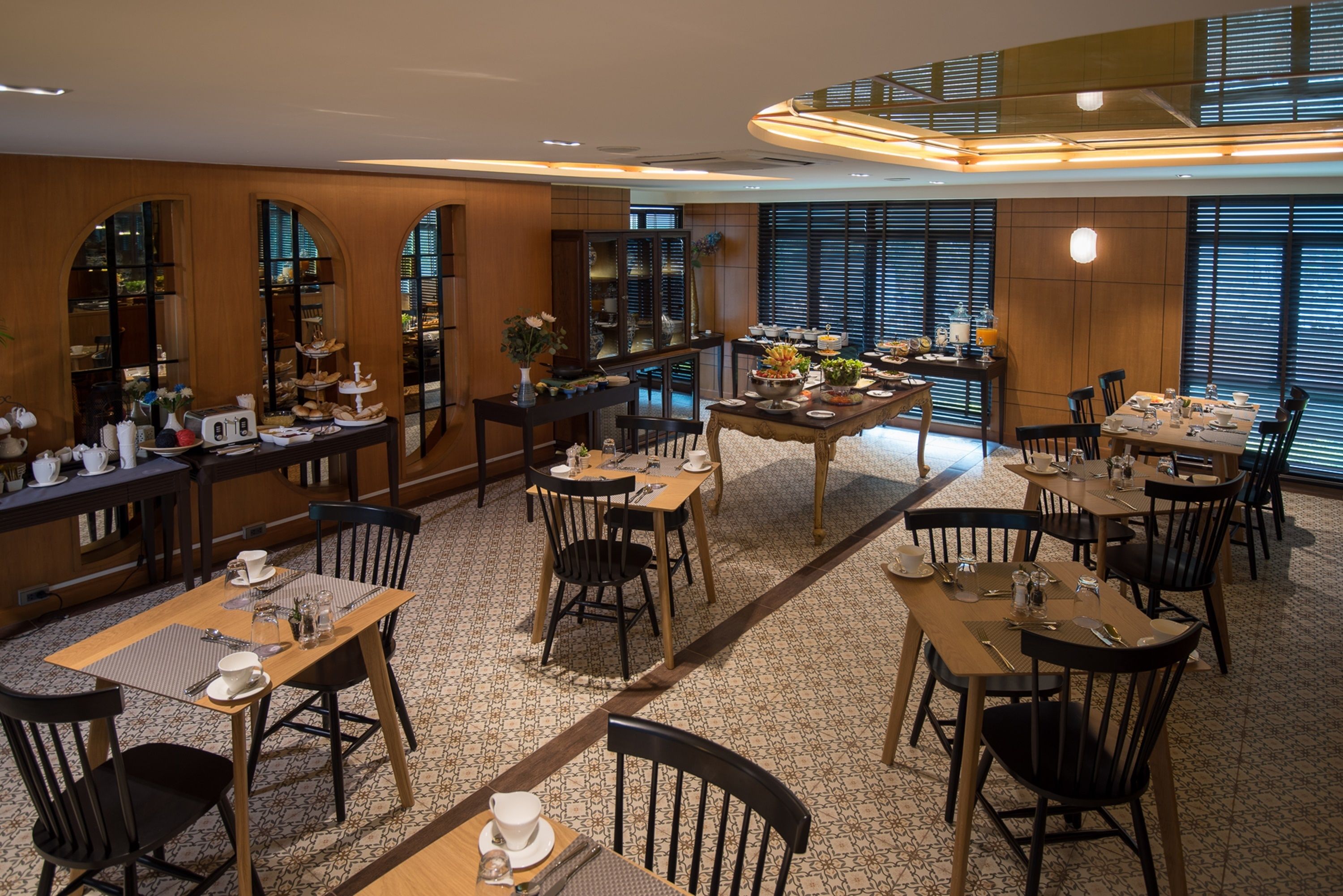A dining area with multiple tables and chairs, wooden paneling, and large windows with blinds.