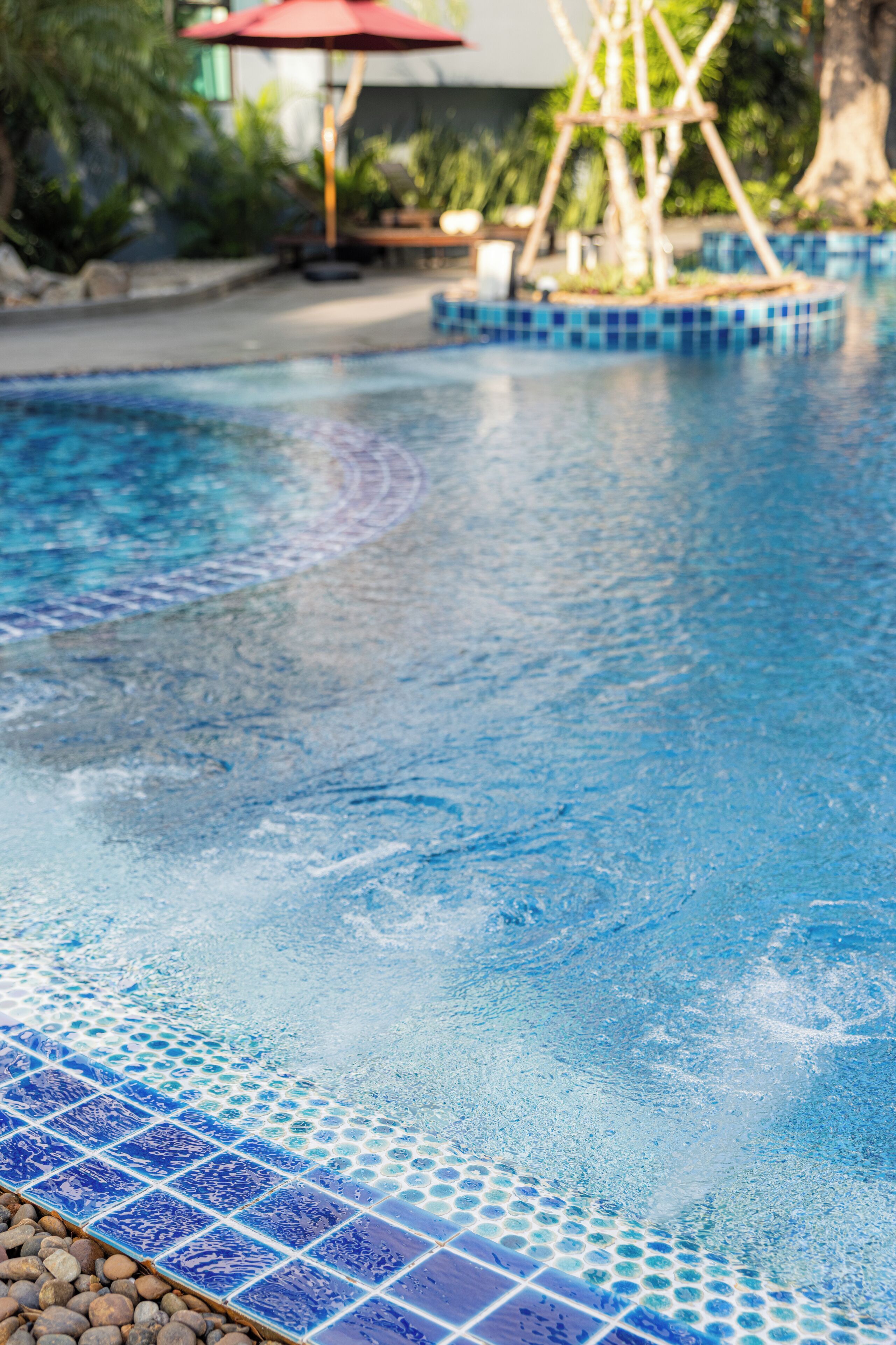 A swimming pool with blue mosaic tiles and a wooden deck area in the background.