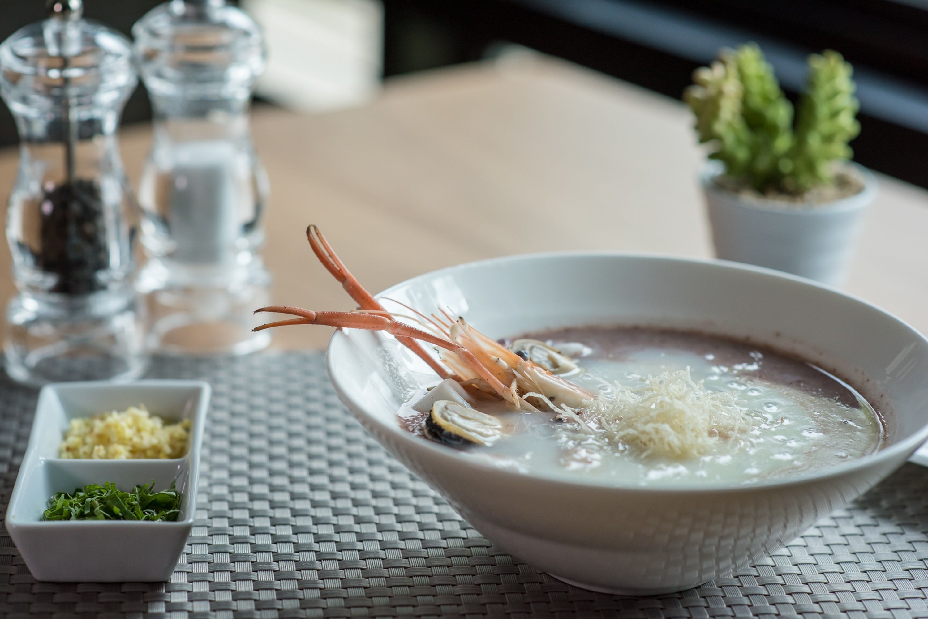 A bowl of soup with seafood, garnished with herbs, on a woven table mat.