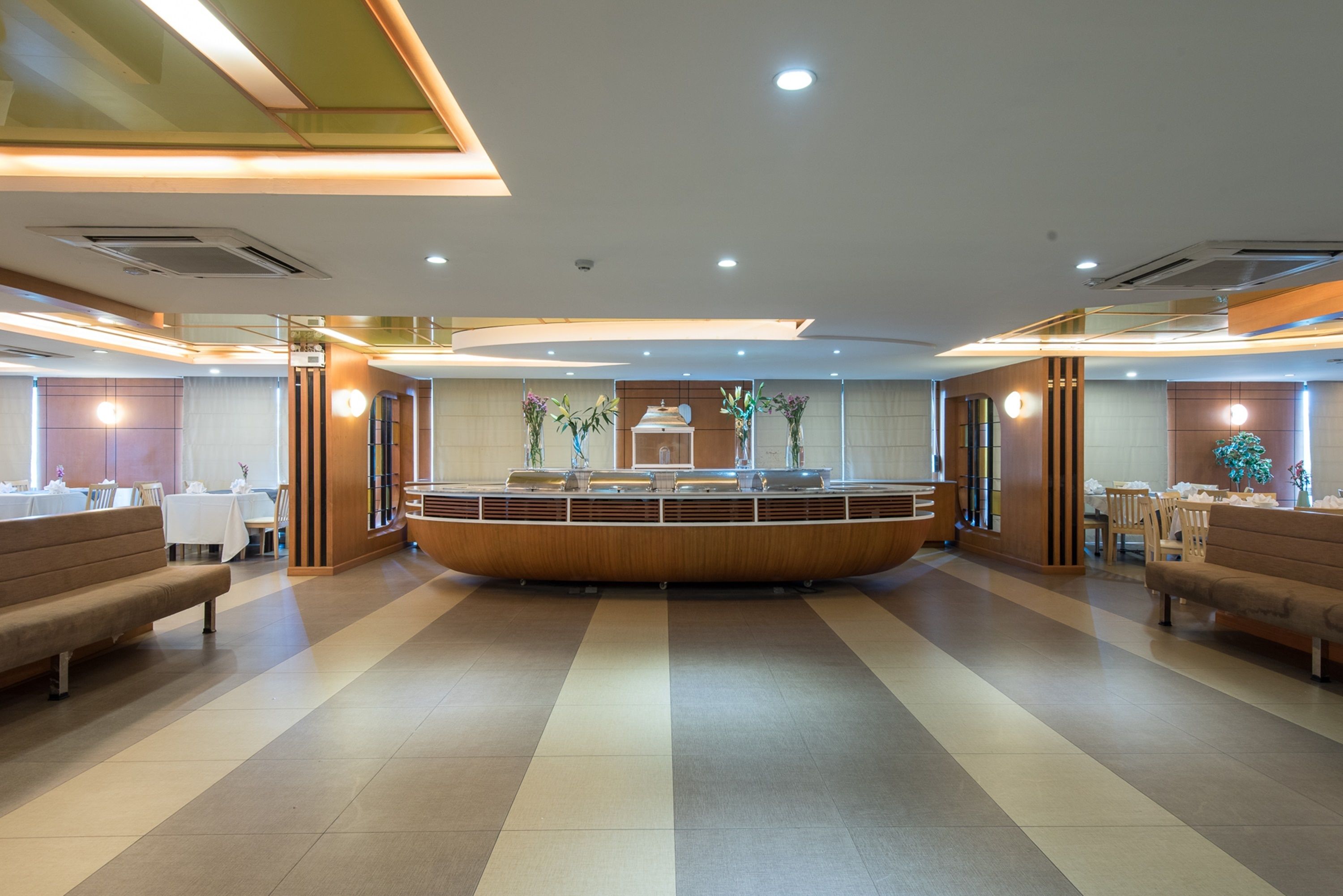 A modern hotel lobby with a central reception desk, seating areas, and a tiled floor.