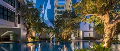 Una piscina interior con suelo de baldosas, rodeada de árboles y edificios modernos con amplias ventanas y un logotipo distintivo azul y blanco.