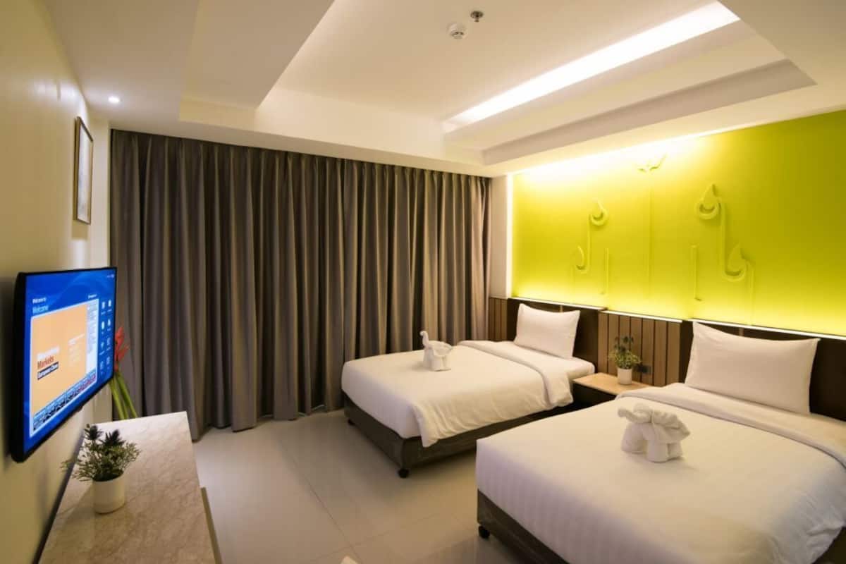 A hotel room with two beds, a flat-screen TV, a desk with a computer, and a bright wall feature.