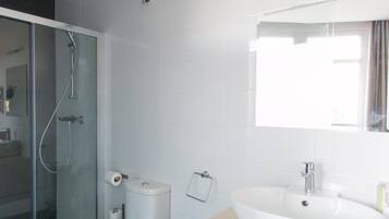 Un baño moderno con cabina de ducha de vidrio, inodoro blanco y un lavabo grande con espejo arriba.
