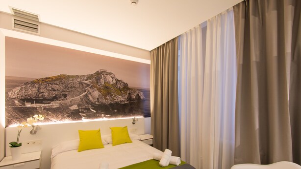 Habitación de hotel con cama, mesita de noche, lámpara y vista a una costa rocosa.