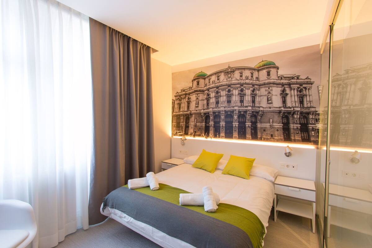 A hotel room with a large bed, a nightstand, a chair, and a wall-mounted TV.