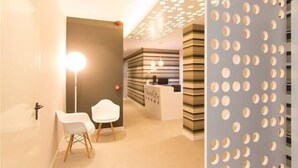 Zona de recepción con diseño moderno, que incluye un mostrador de recepción, dos sillas blancas y un muro con estampado.