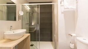 Un baño moderno con ducha de vidrio, lavamanos blanco y un inodoro.