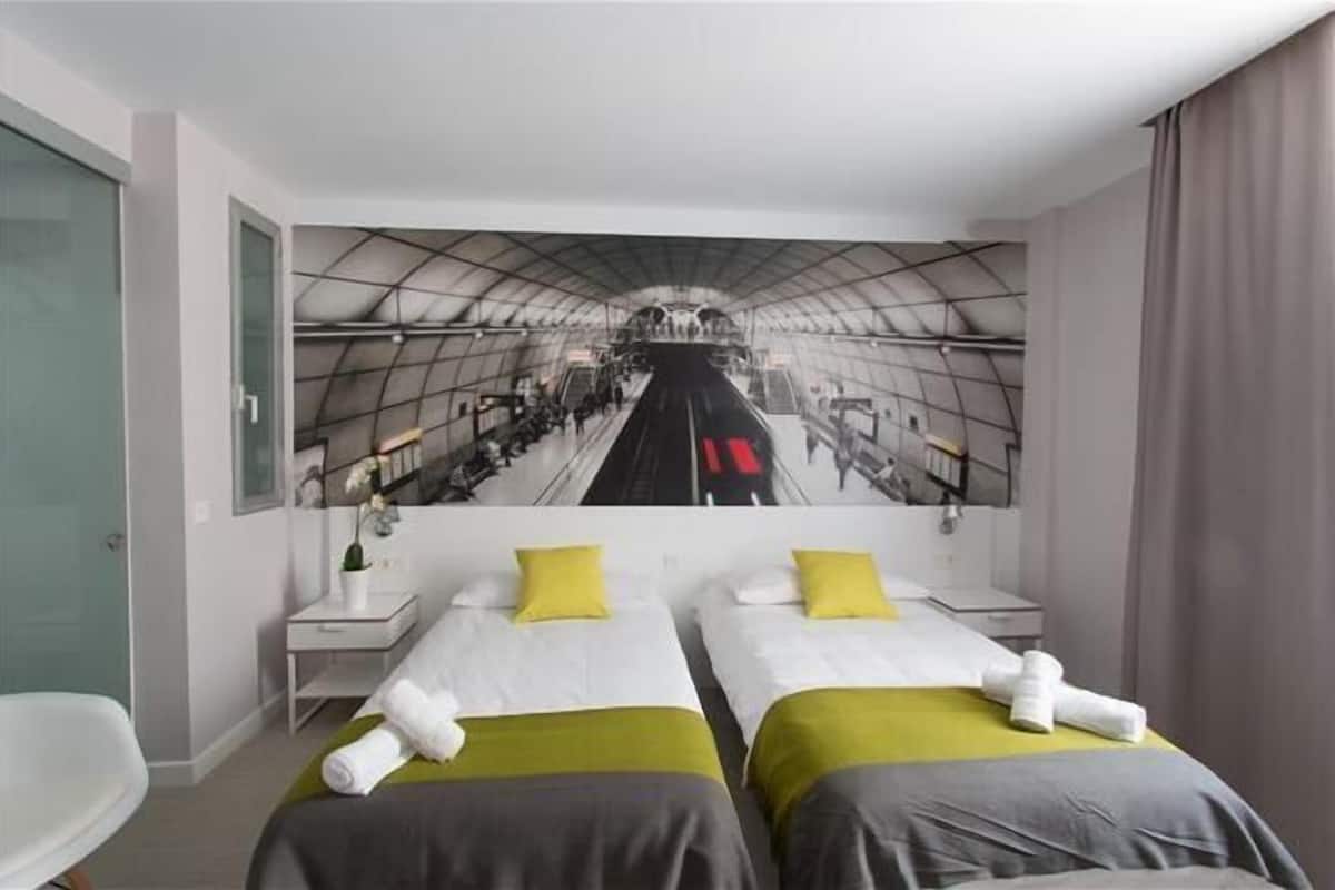 A hotel room with two beds, a large mural of a train, a small desk, and a chair.