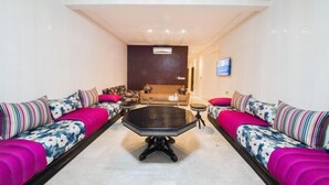 A spacious living room with a central coffee table, sofas with floral upholstery, and a dark-colored accent table. - Apartment 3 Rooms city center Fes (Fes)