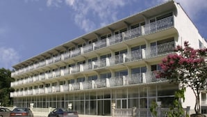 Un hôtel à plusieurs étages, doté de balcons à chaque niveau, de grandes fenêtres et d’un espace de stationnement à l’avant.