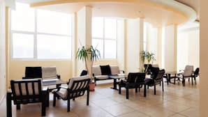 Un espace intérieur spacieux, doté de nombreuses tables et chaises, de grandes fenêtres laissant entrer la lumière naturelle et de plantes en pot.