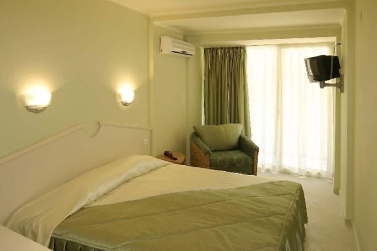 Una habitación de hotel con una cama, una silla y un televisor montado en la pared.