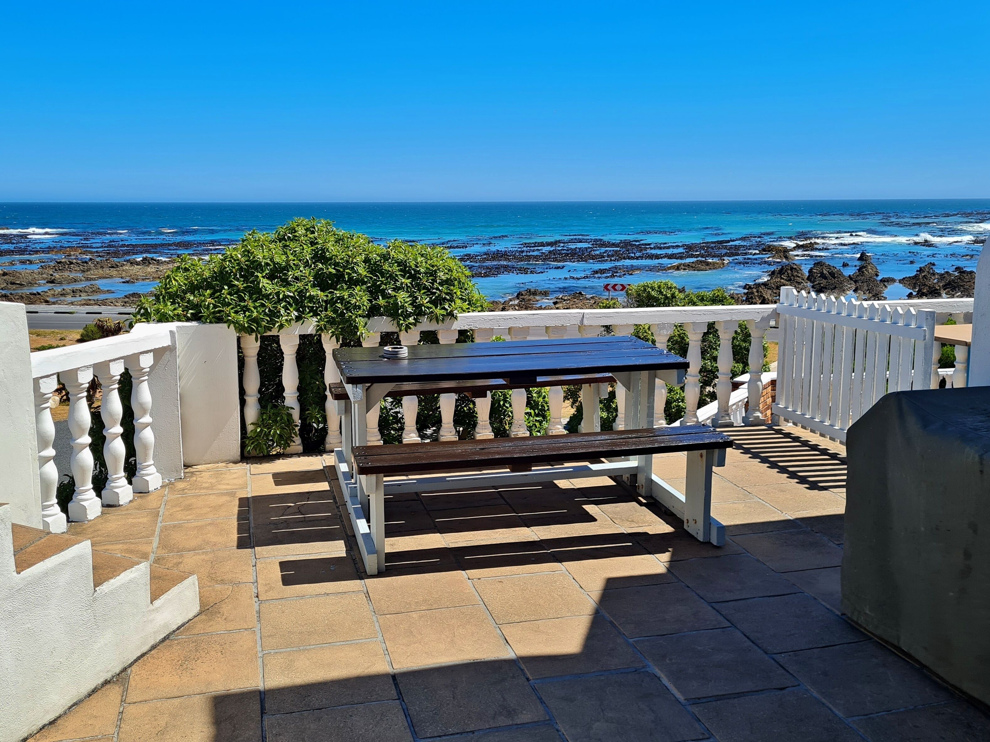 A patio with a table and benches overlooking a rocky coastline.