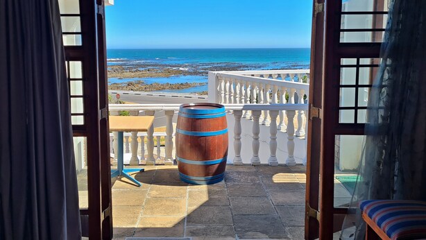 Un balcón con vista al mar, un barril de madera y una barandilla blanca.