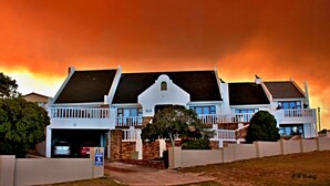 Una casa grande de dos pisos con garaje, rodeada por una cerca blanca, bajo un cielo naranja intenso.
