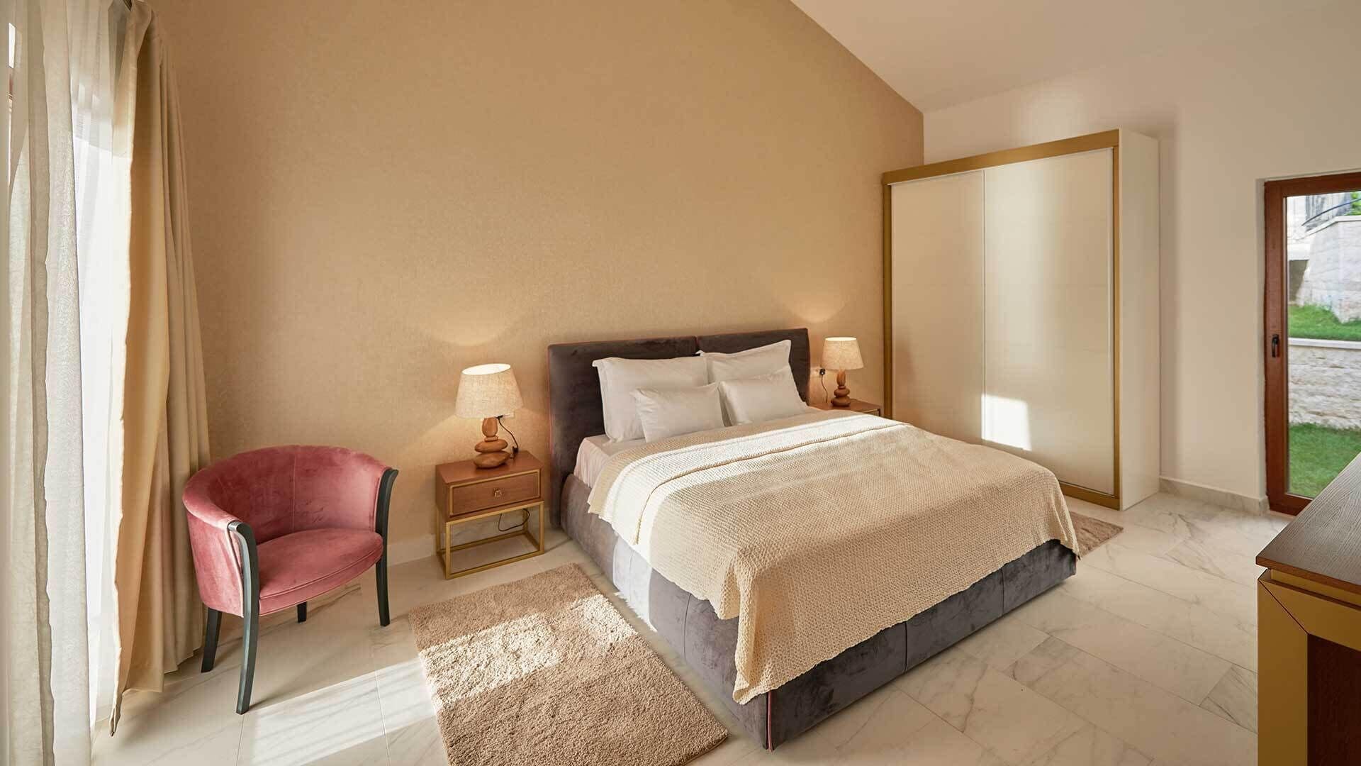 Un dormitorio con cama, mesitas de noche, una silla y vistas al exterior.