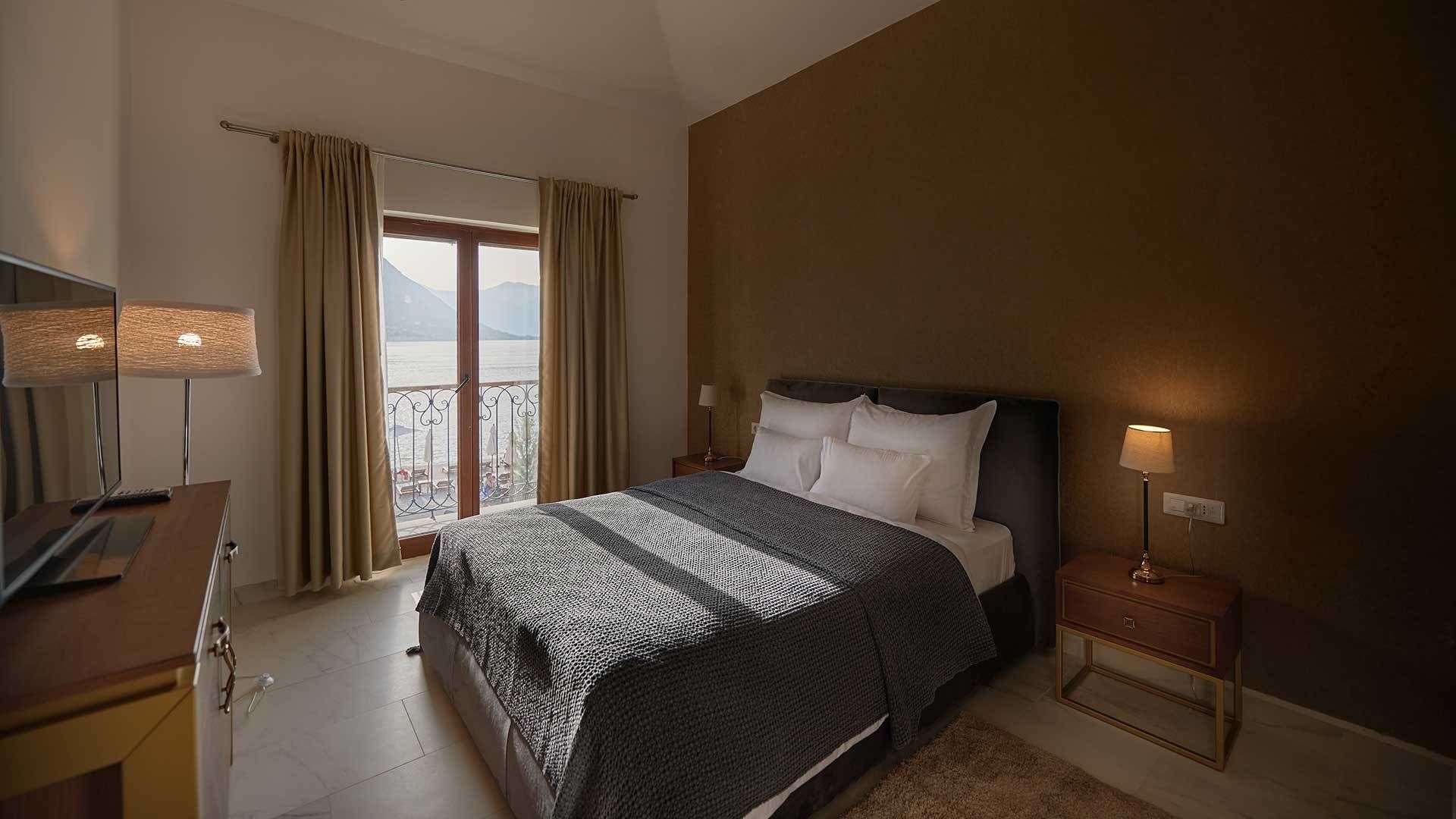 A hotel room with a bed, bedside tables, a desk, and a view of the sea.