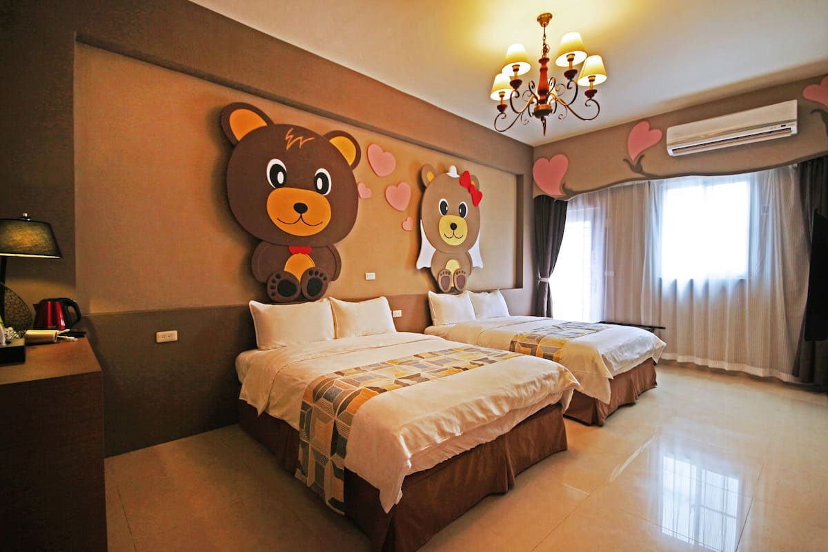 A hotel room with two beds, a chandelier, an air conditioner, and a large bear decoration on the wall.