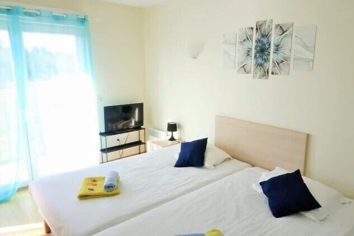 Habitación de hotel con dos camas, televisión, lámpara y una obra de arte en la pared.