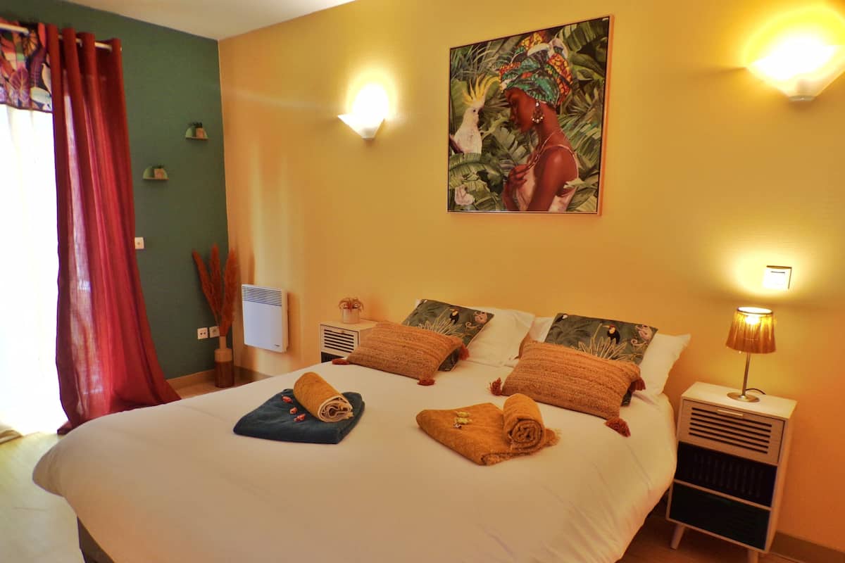Una habitación de hotel con una cama grande, dos lámparas de noche, un cuadro en la pared y una mesita con una lámpara.