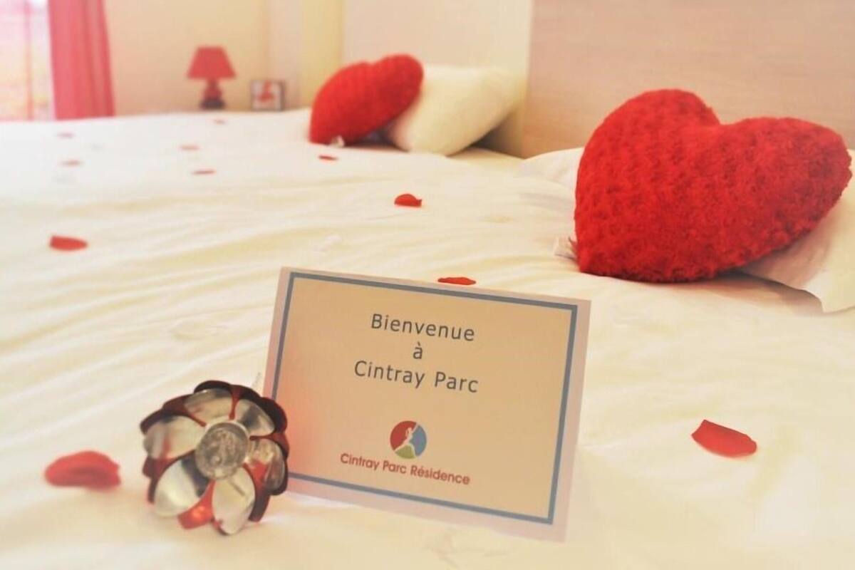 Una cama con almohadas rojas con forma de corazón y un cartel de bienvenida que dice "Bienvenue à Cintray Parc".